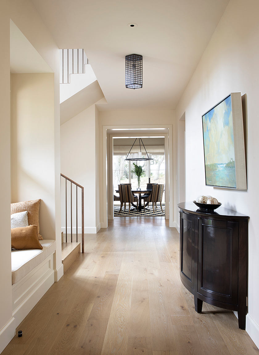 A modern, light-filled hallway with a geometric light fixture, wood floors, and a painted staircase.