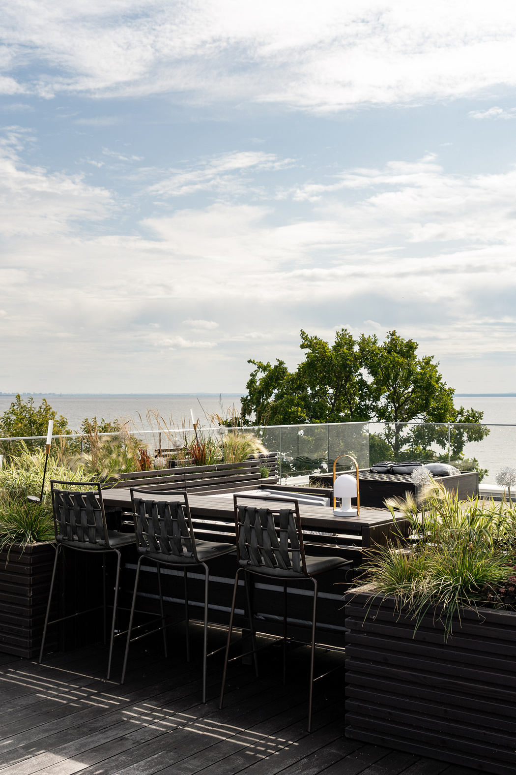 Sleek outdoor patio with black modern furniture, glass railings, and lush greenery.