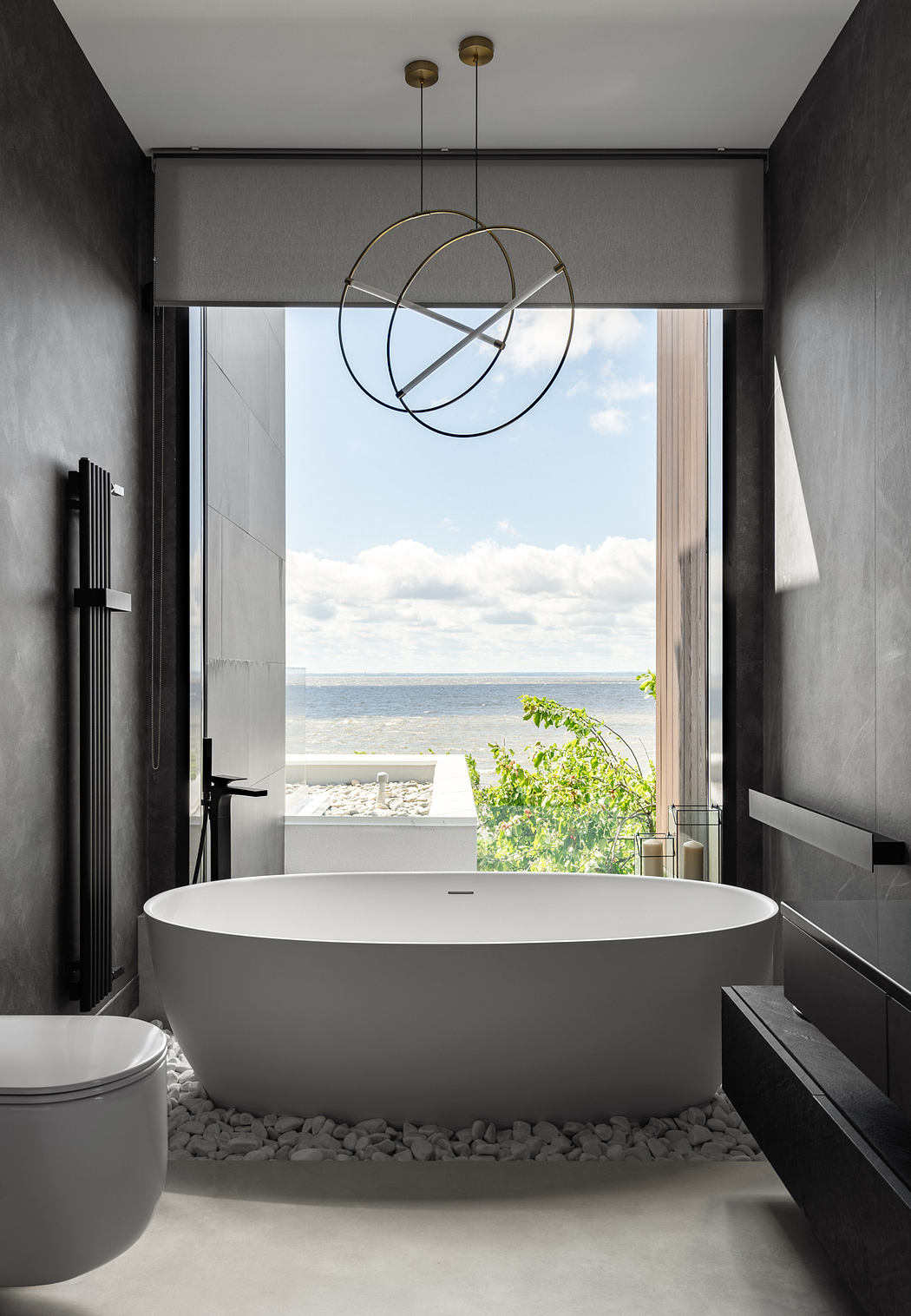 A modern, minimalist bathroom with a freestanding tub, rings pendant light, and scenic beach view.