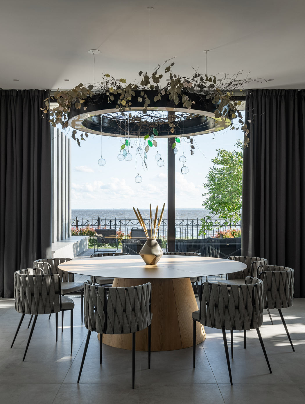 A modern dining room with a striking round chandelier and a panoramic view of the outdoors.