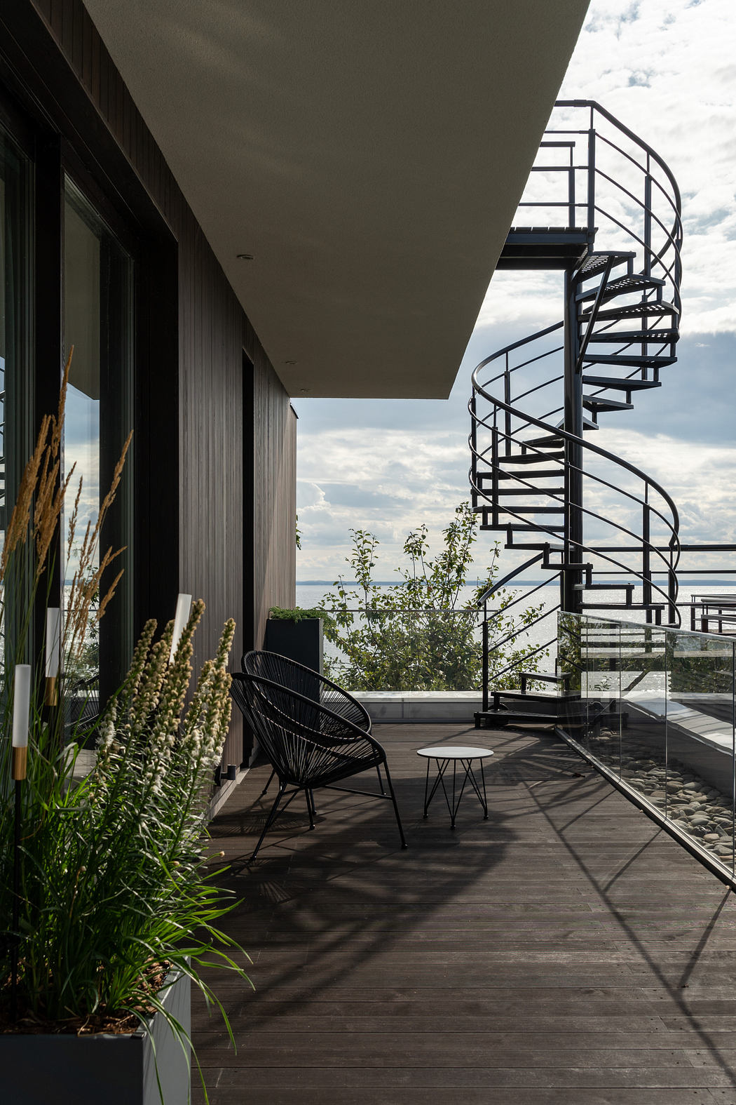 A modern exterior with a spiral staircase, outdoor seating, and lush greenery.