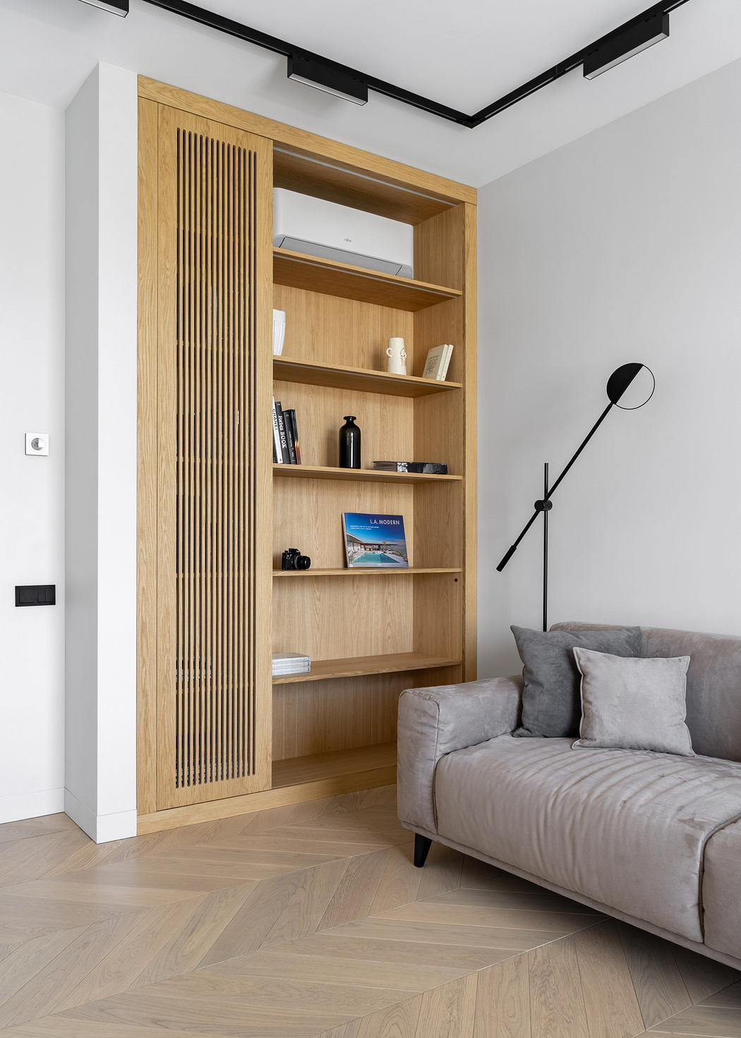 Minimalist living room with a wooden built-in shelving unit, grey sofa, and stylish floor lamp.