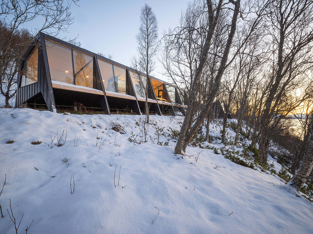 A modern, glass-walled cabin nestled in a snowy forest, with warm lighting inside.
