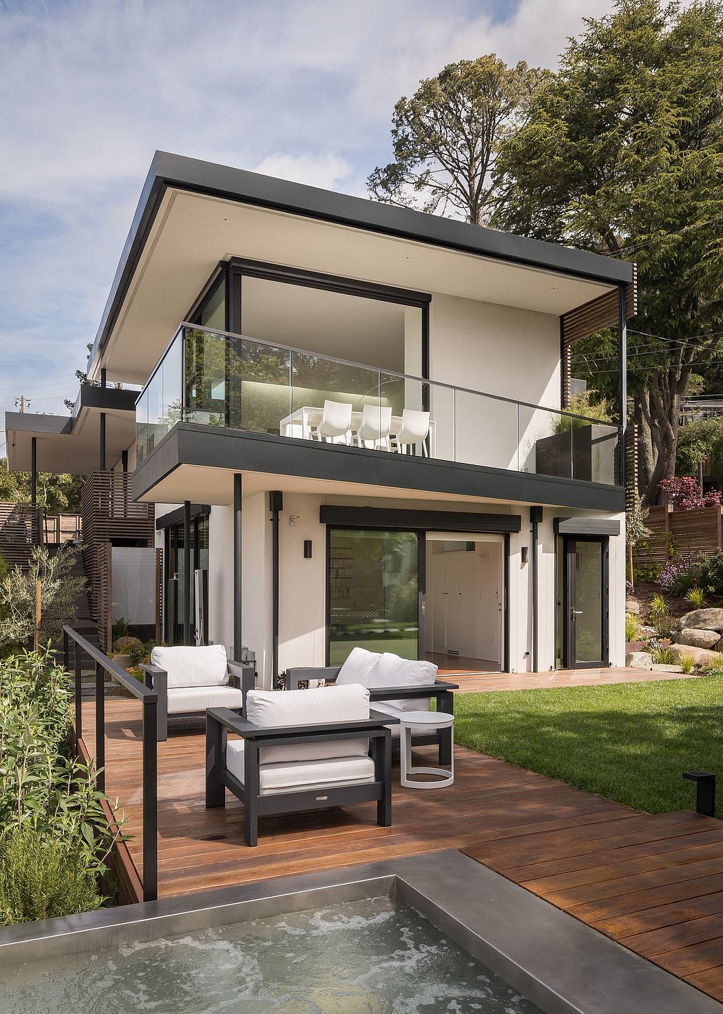 Modern two-story home with glass walls, wooden deck, and serene outdoor space.