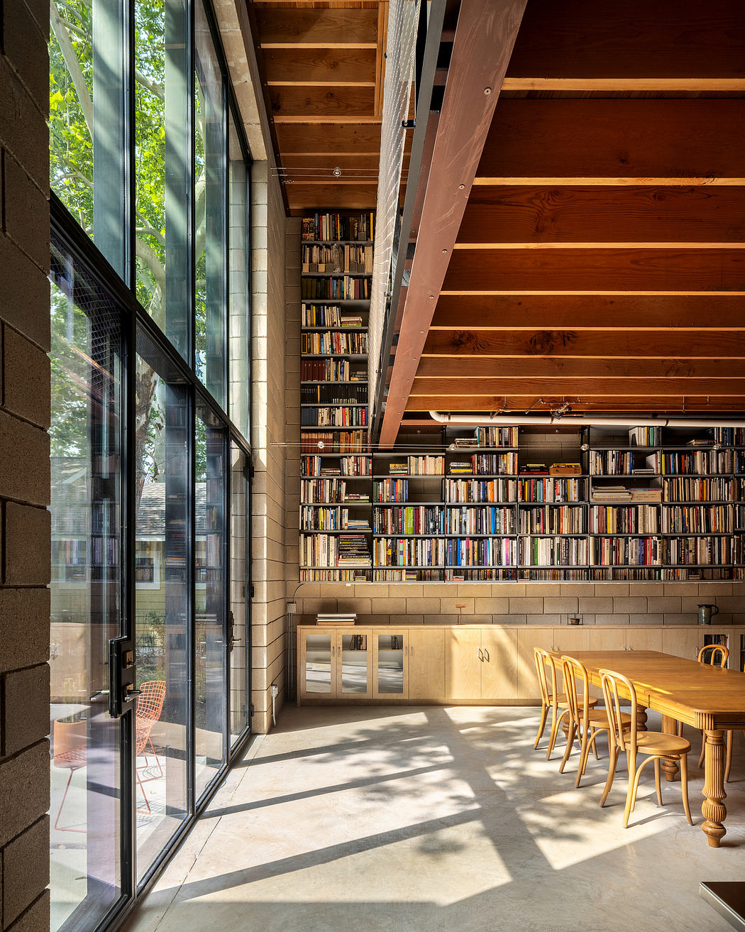 Sprawling wooden shelves and a cozy reading nook with floor-to-ceiling windows overlooking nature.
