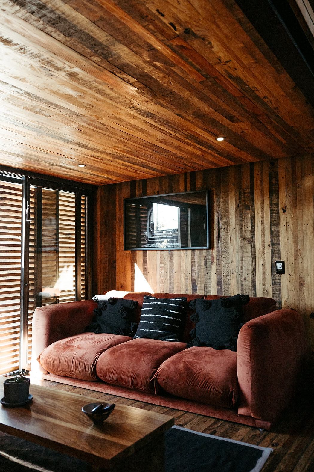 Cozy rustic living room with wooden walls, plush velvet sofa, and recessed lighting.