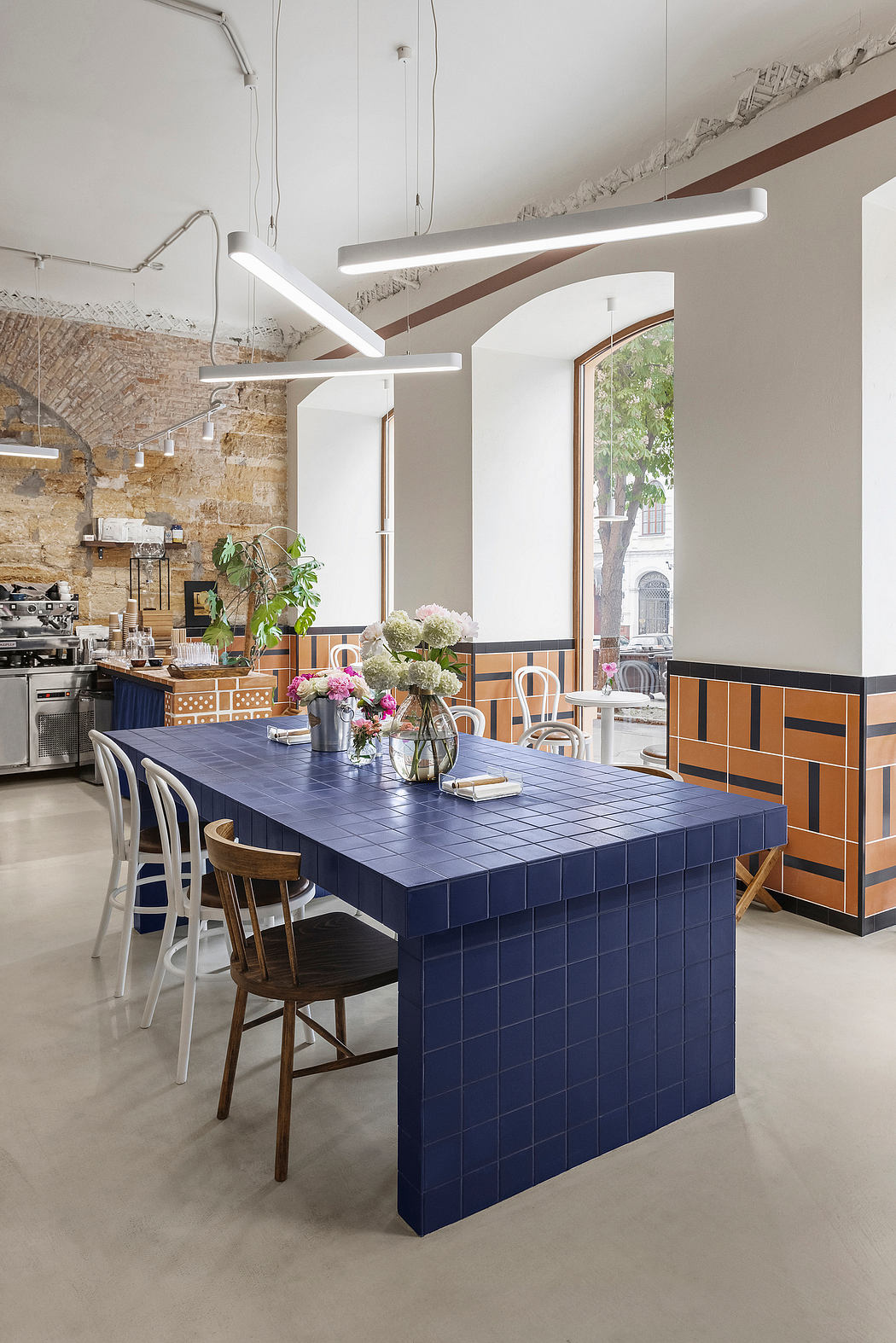 A modern, tile-accented kitchen with a bold, blue central dining table and pendant lights.