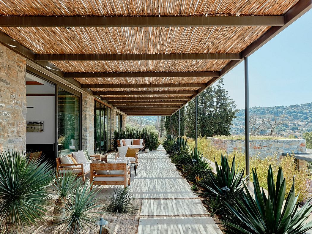 Rustic patio with thatched roof, stone walls, and lush vegetation overlooking a scenic landscape.