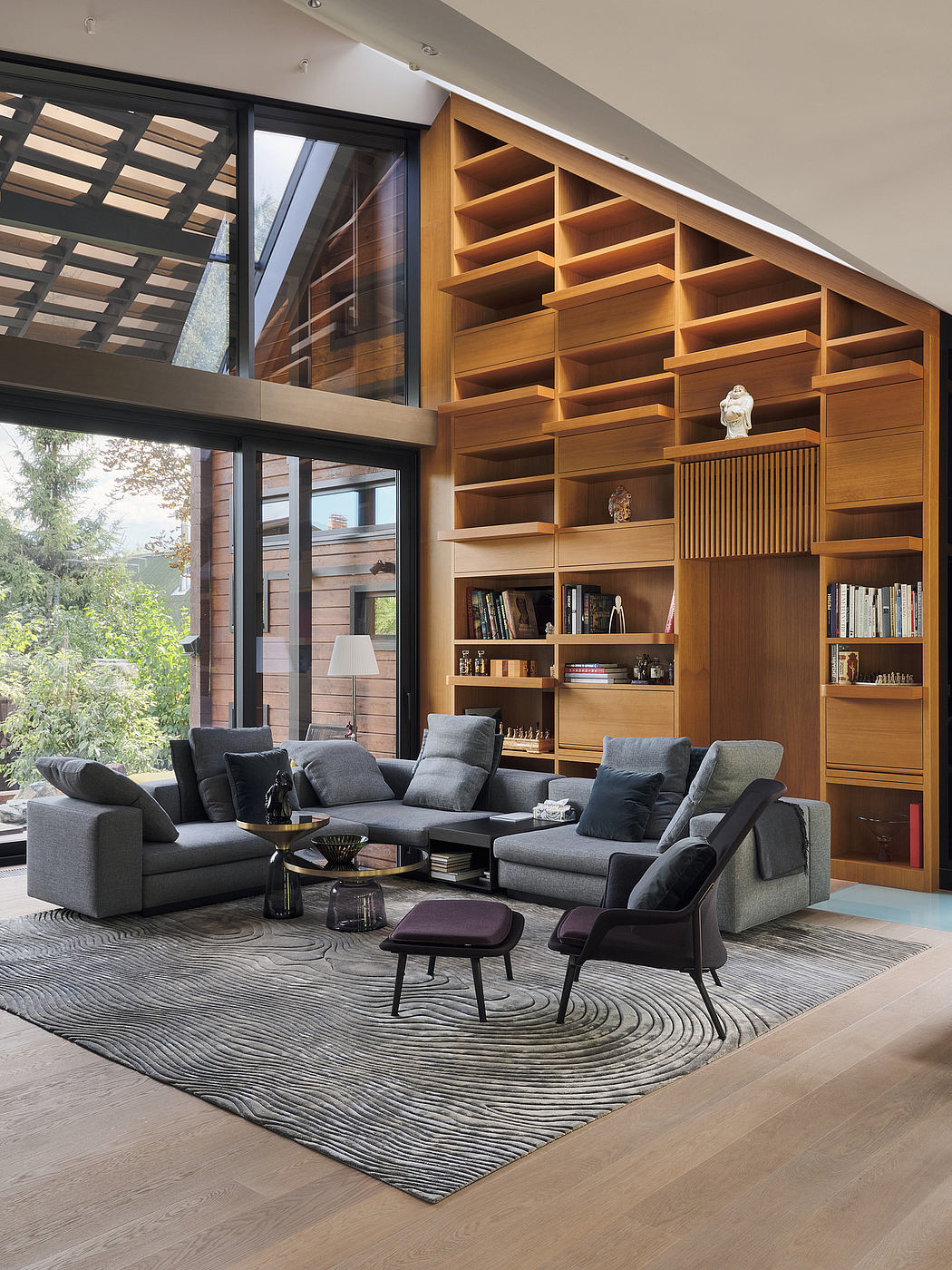 Spacious living room with towering wooden shelving, plush gray sofas, and geometric rug.