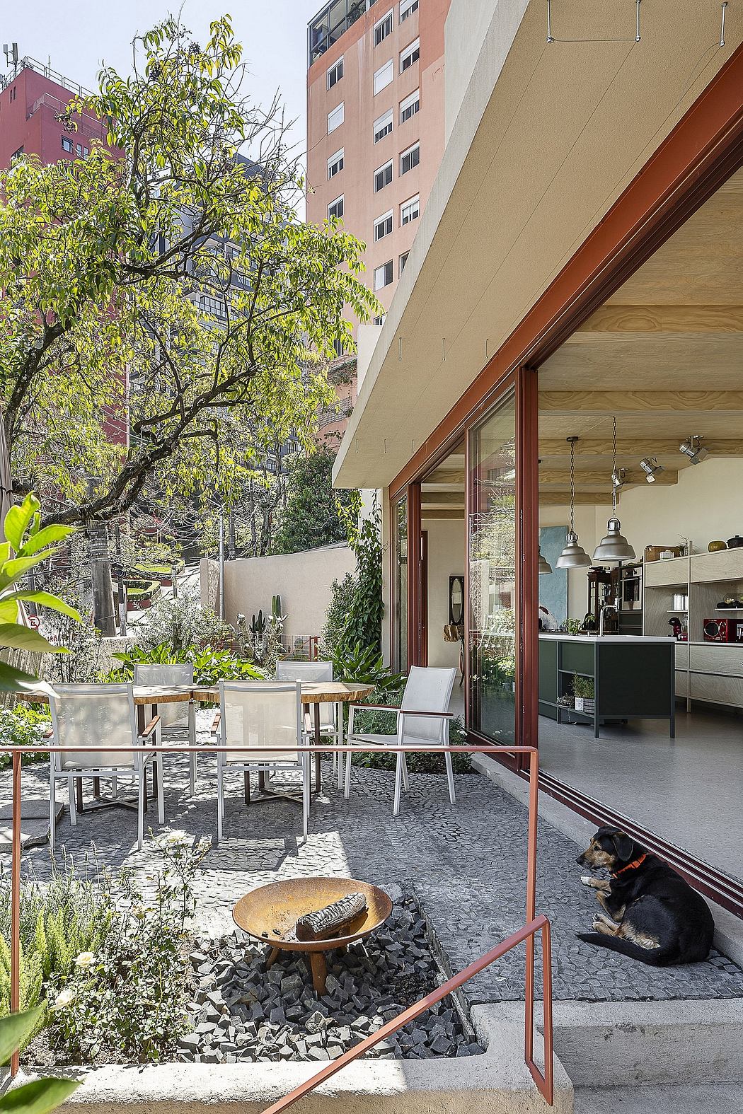 An outdoor dining area with modern architectural elements, surrounded by lush greenery.