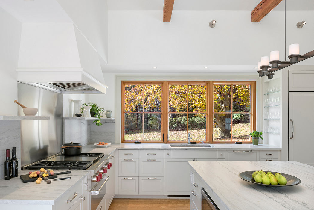 Bright modern kitchen with wood beams, large windows overlooking autumn trees.
