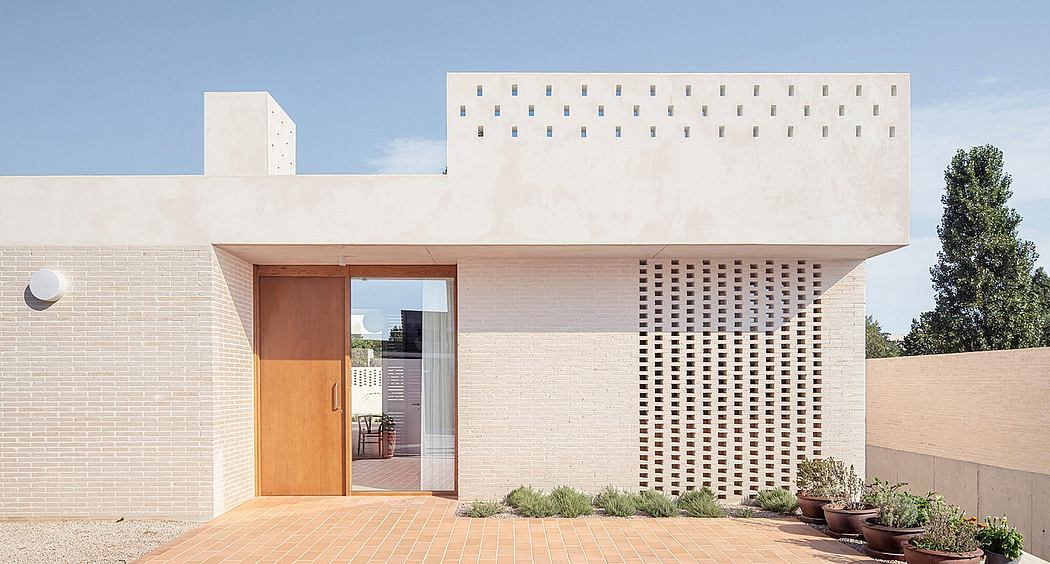 A modern, minimalist building with geometric patterns, wooden doors, and a tiled patio.