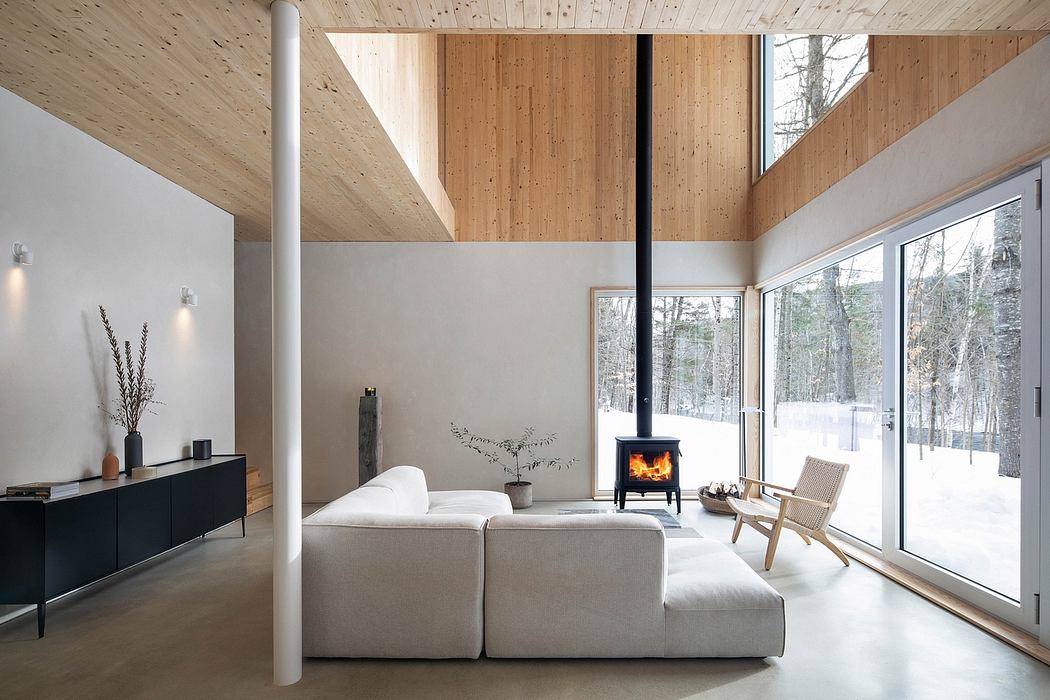 A cozy living room with wood-paneled walls, a fireplace, and large windows overlooking a snowy landscape.
