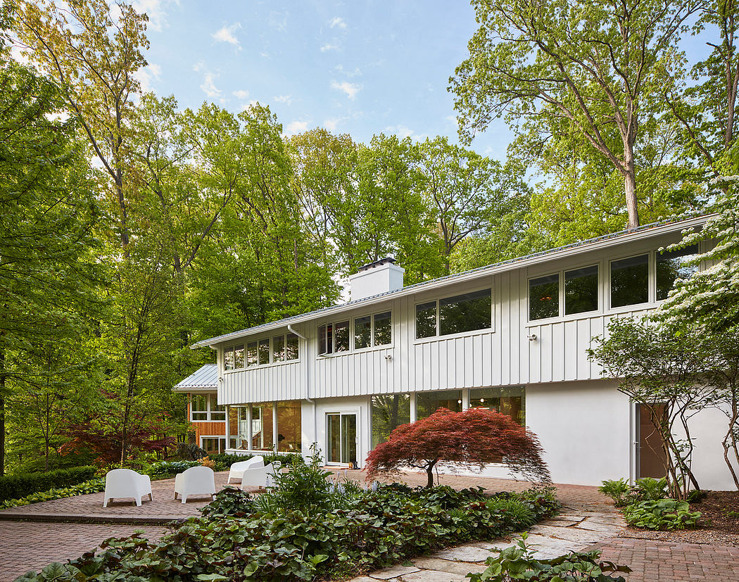 Modern, single-story house with large windows, surrounded by lush greenery and a landscaped garden.