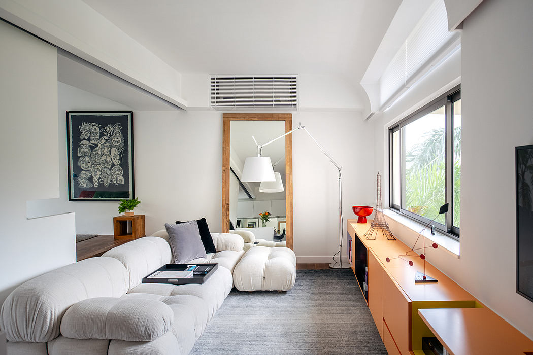 A modern, minimalist living room with white sofas, wooden furniture, and artwork on the walls.