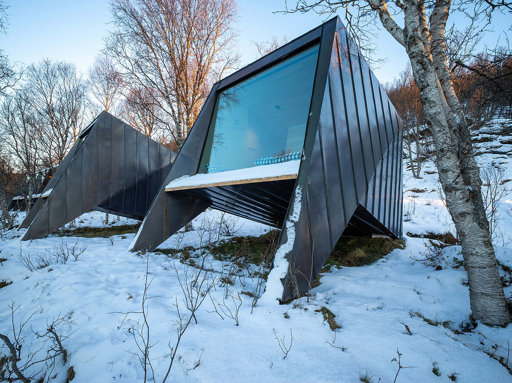 A modern and angular glass-walled structure nestled in a snowy, forested landscape.