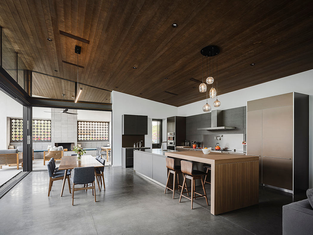 A modern kitchen and dining area with a wooden ceiling, pendant lights, and minimalist decor.