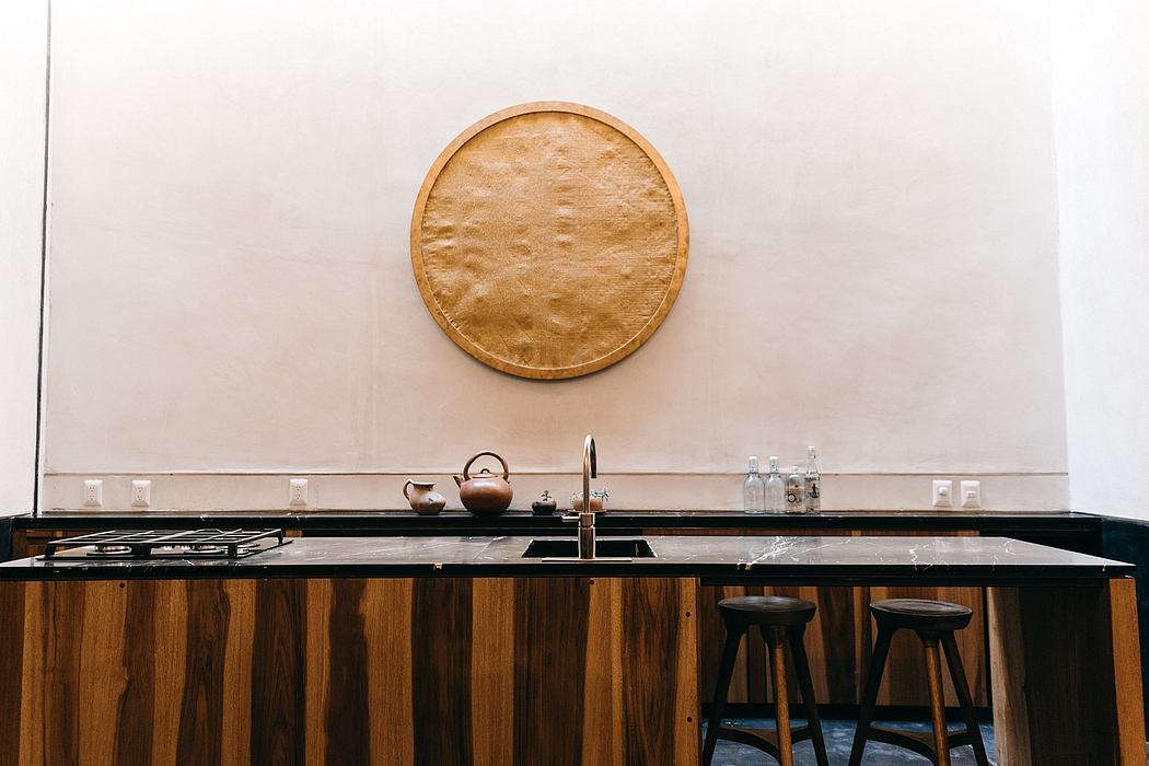 Modern minimalist kitchen with large circular mirror, wooden cabinetry, and sleek black countertops.