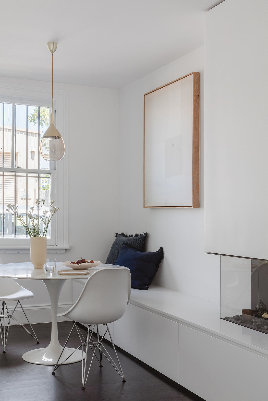 Minimalist dining area with pendant light, wooden framed artwork, and built-in storage.