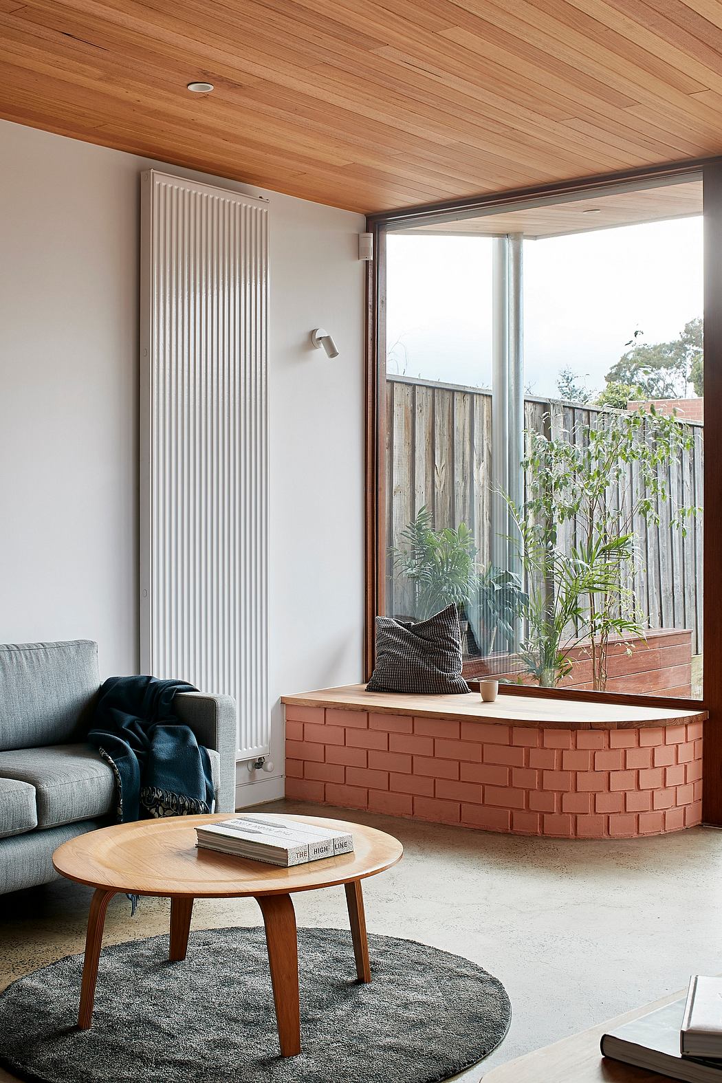 Cozy mid-century living room with wood ceiling, brick planter, and modern furnishings.