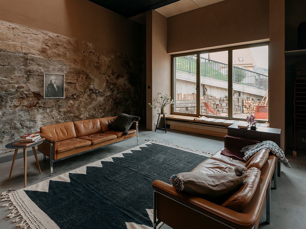 Rustic living room with exposed stone wall, leather furniture, and large window offering outdoor view.