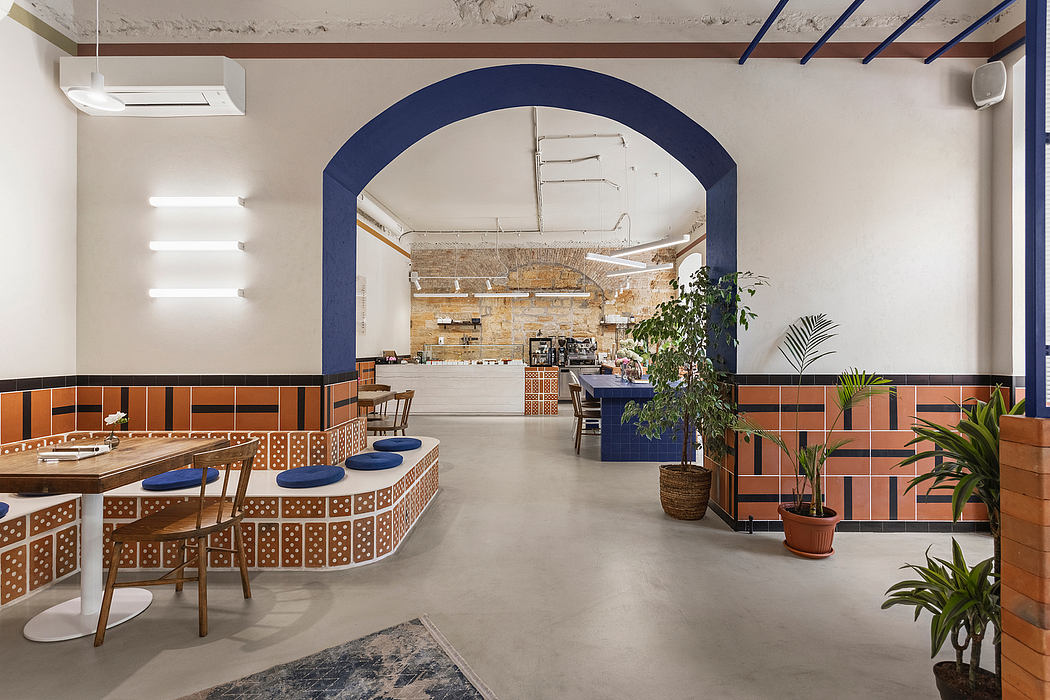 Modern, cozy cafe interior with arched entryway, colorful tiled accents, and lush greenery.