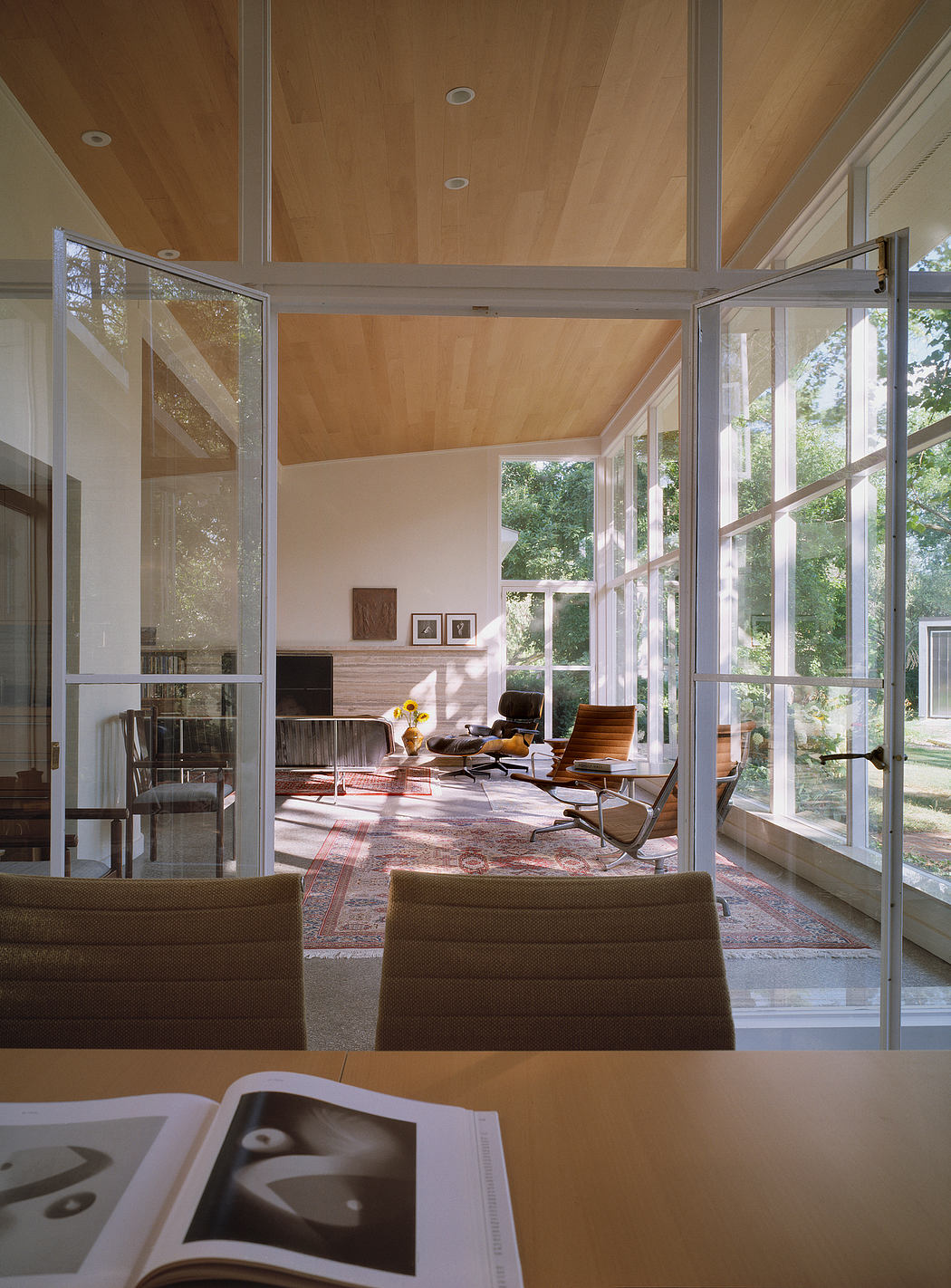 Modern sunlit living room with vaulted wood ceiling, large windows, and mid-century furnishings.