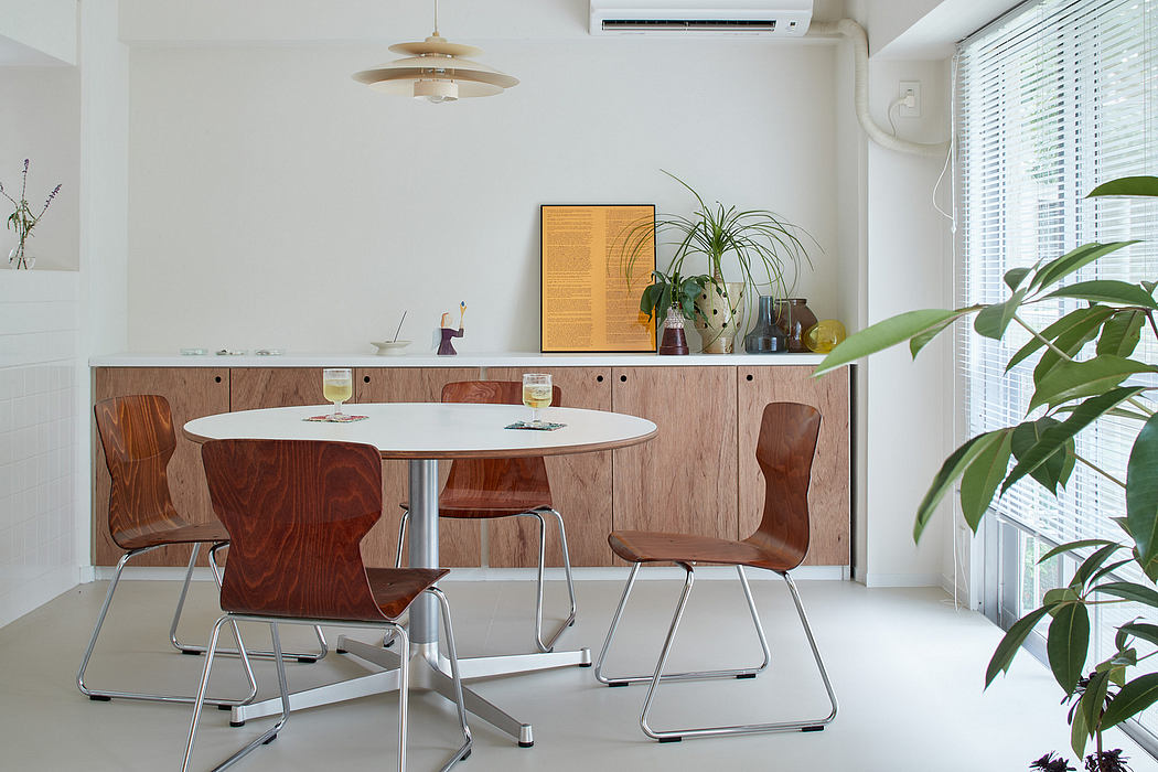 Modern dining room with circular table, wooden chairs, and potted plants near window.