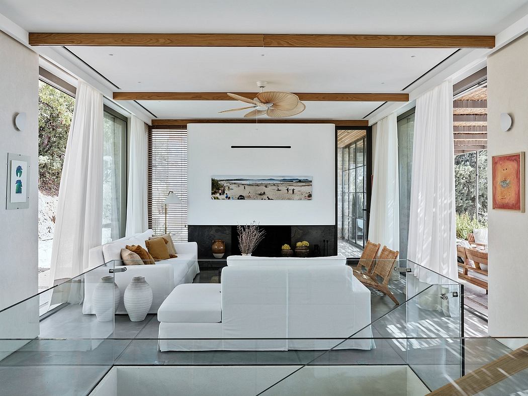 Spacious living room with wooden beams, white sofas, and a large glass wall overlooking nature.