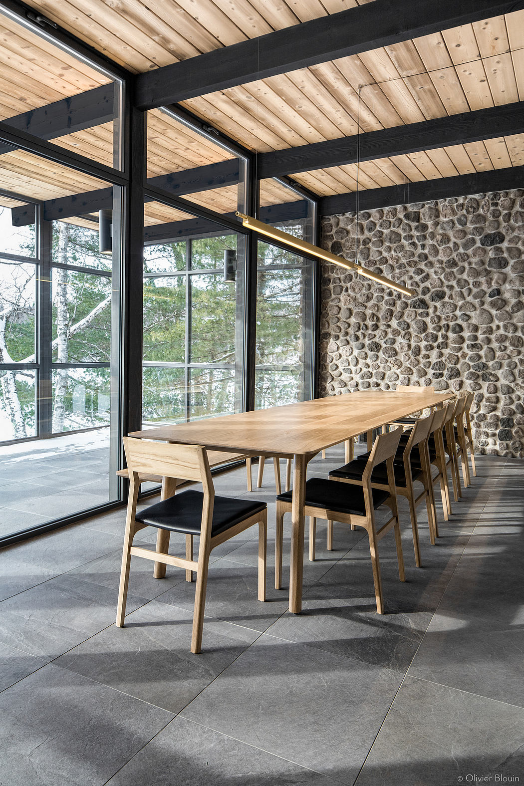 Rustic wood-beamed ceiling, stone wall, and floor-to-ceiling glass windows create a cozy dining area.