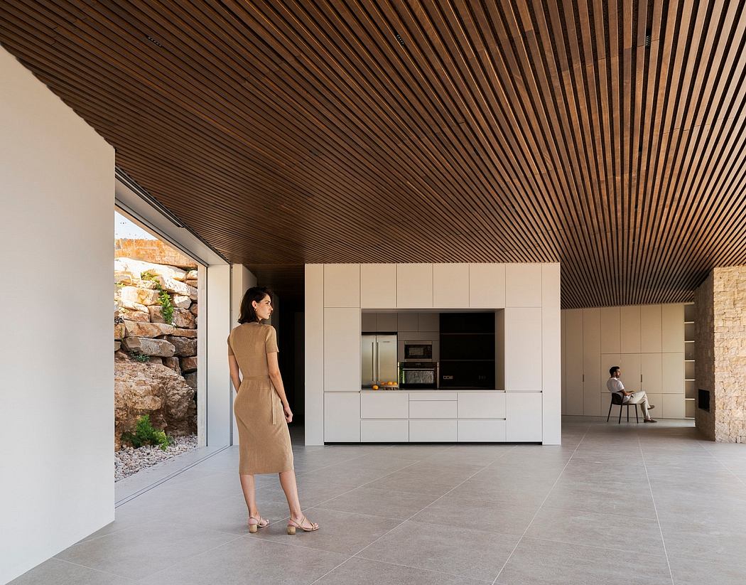 The image showcases a modern, minimalist interior design with a striking wooden ceiling and built-in kitchen cabinets.