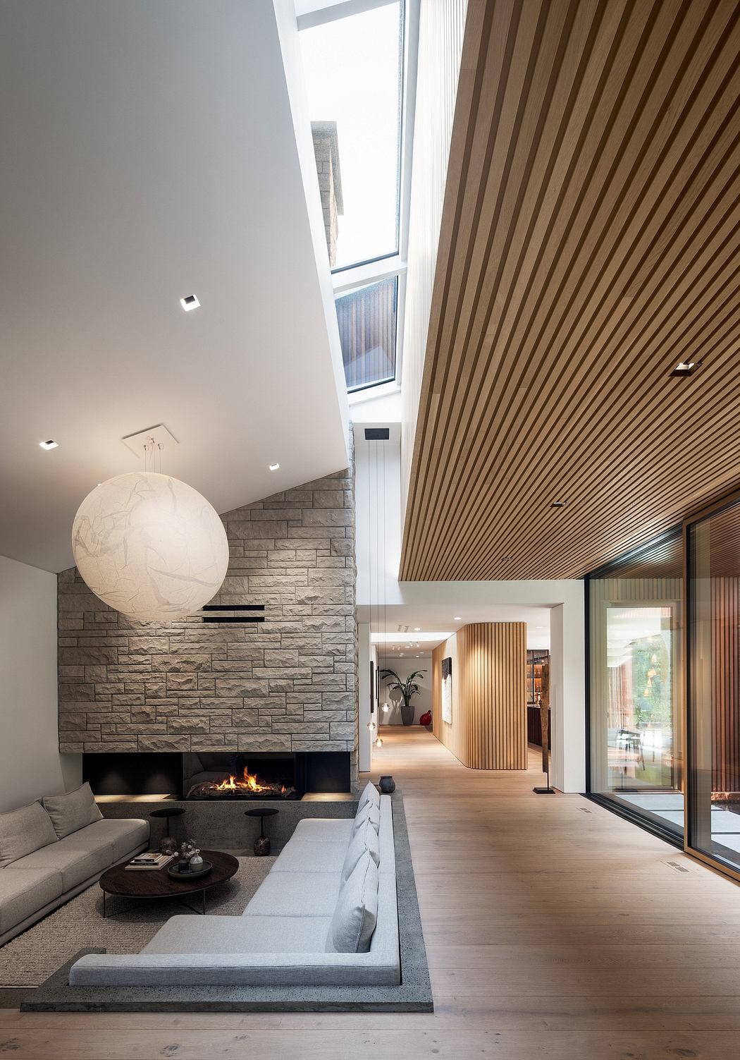 Spacious modern living room with stone fireplace, wood paneled ceiling, and large windows.
