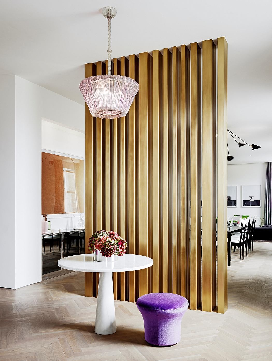 Elegant dining room with striking metallic divider, plush purple stool, and crystal chandelier.