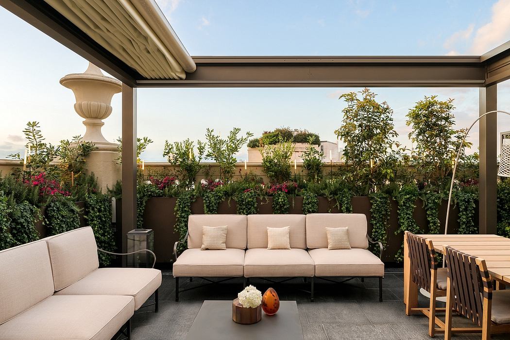 A cozy outdoor terrace with lush greenery, a plush sofa, and a wooden dining set, framed by an ornate canopy.