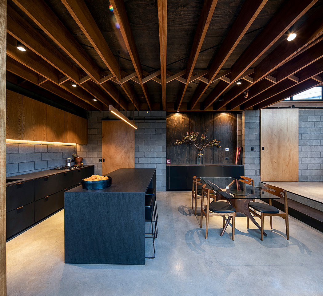 A modern, open-concept kitchen with a sleek, dark-colored island and wooden ceiling beams.