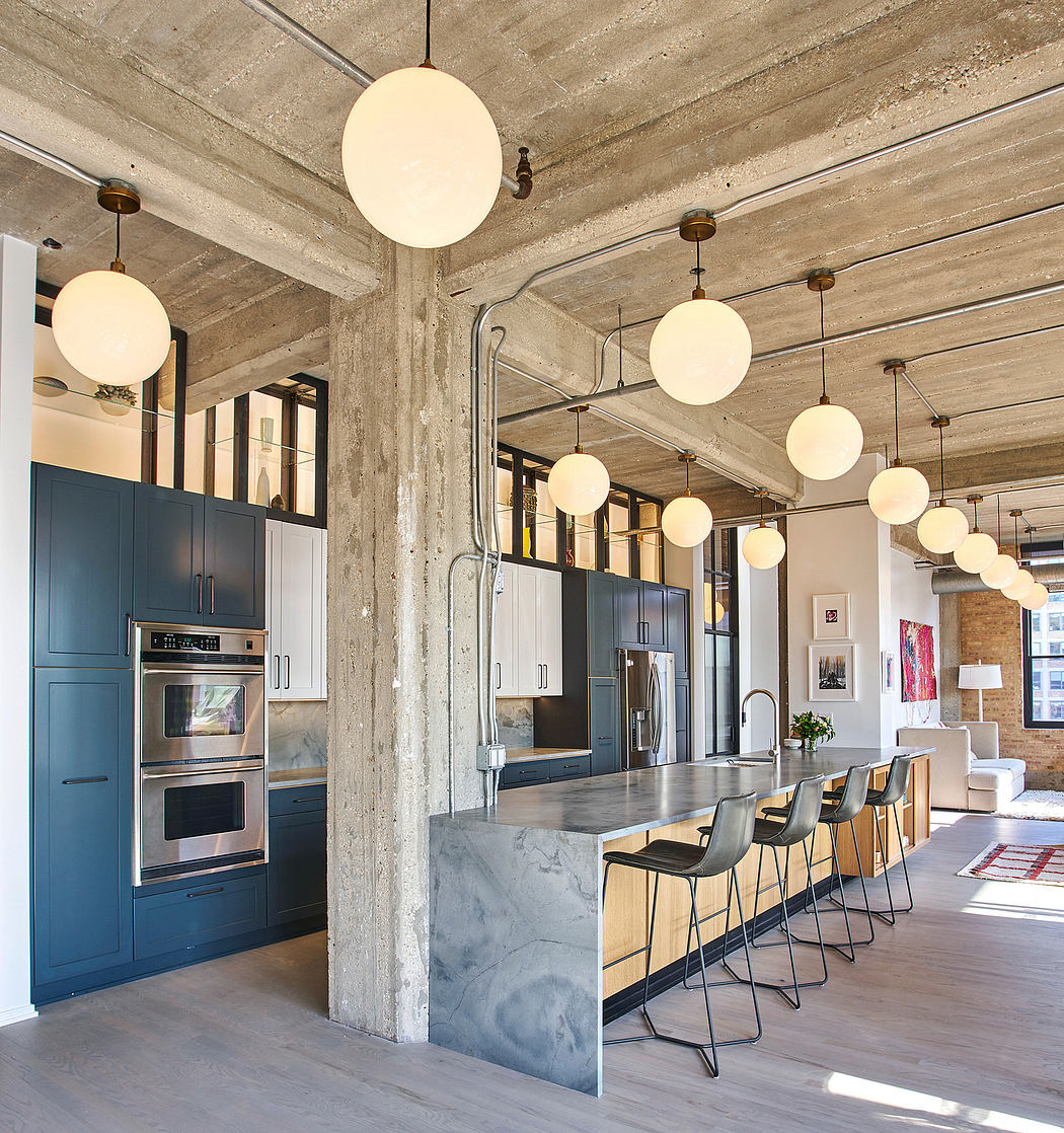 This open-concept kitchen features a modern, industrial aesthetic with exposed concrete walls and globe pendant lights.