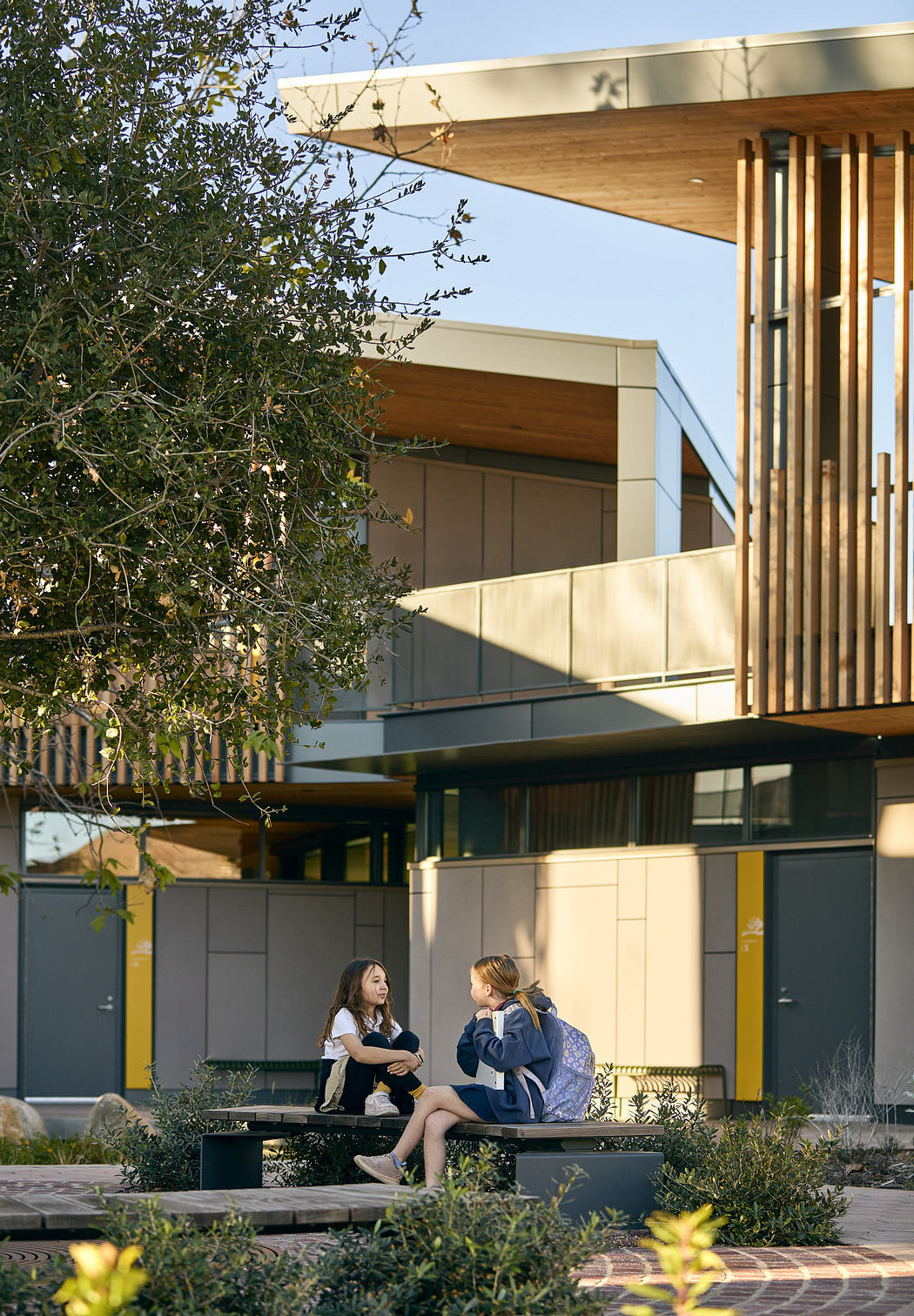 The image shows a modern, well-designed building with clean lines, wooden accents, and a covered outdoor seating area.