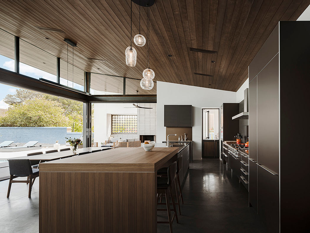 Spacious modern kitchen with wooden paneled ceiling, pendant lights, and expansive island.