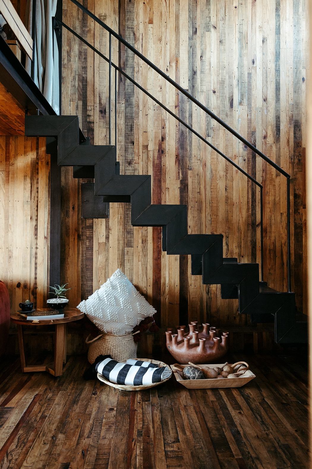 A rustic staircase with black metal steps against a wooden wall backdrop, complemented by decor.