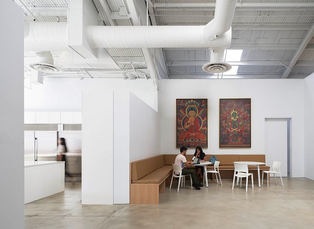Modern open-concept workspace with hanging pipes, colorful artwork, and casual seating.
