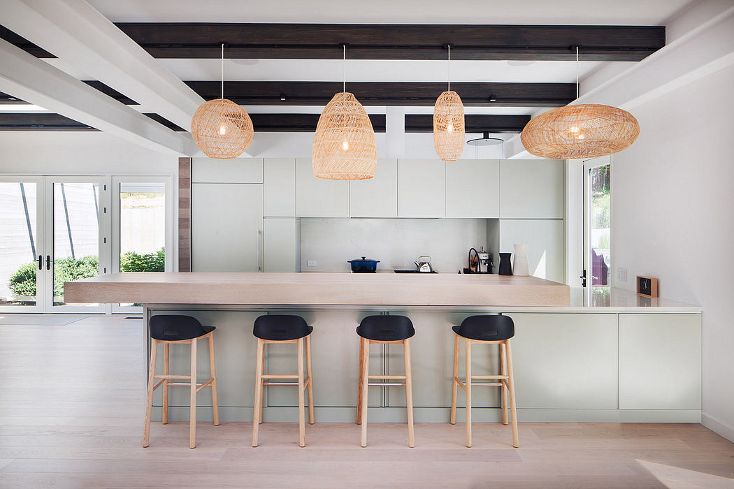 A modern kitchen with sleek, minimalist design, featuring rattan pendant lights and bar stools.
