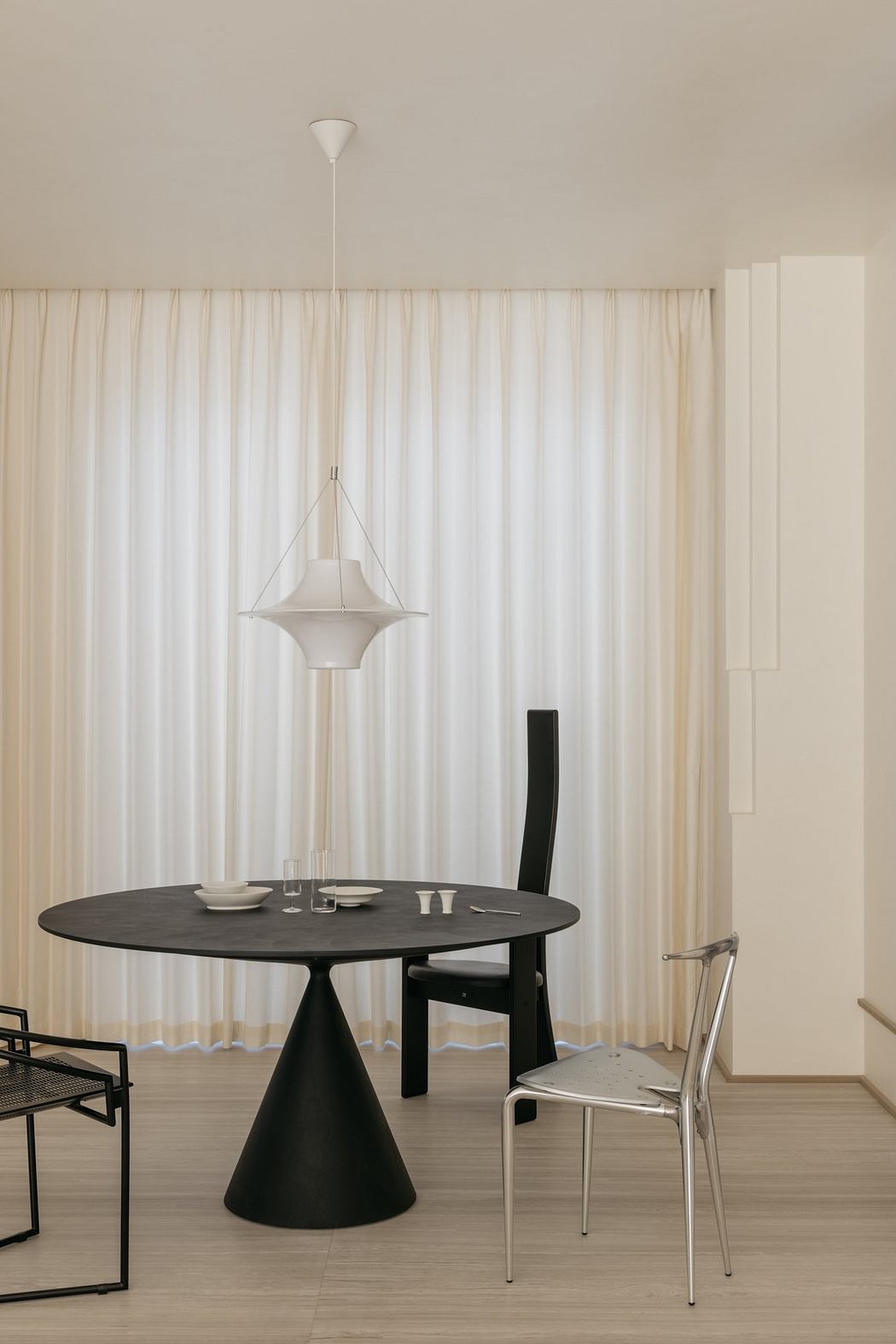 Minimalist dining room with a circular black table, modern pendant light, and sleek furnishings.