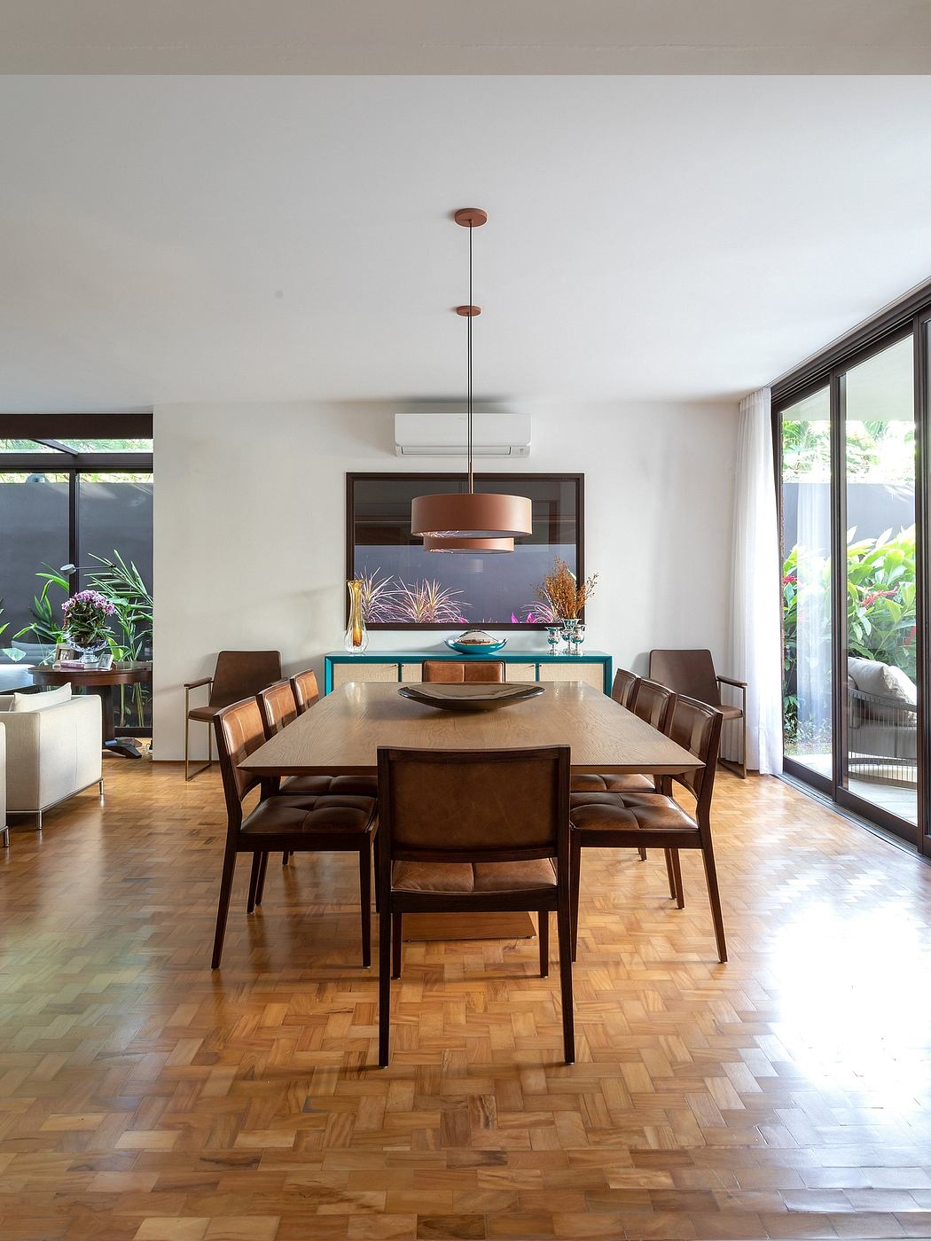 A modern dining space with wooden furnishings, statement lighting, and lush greenery.