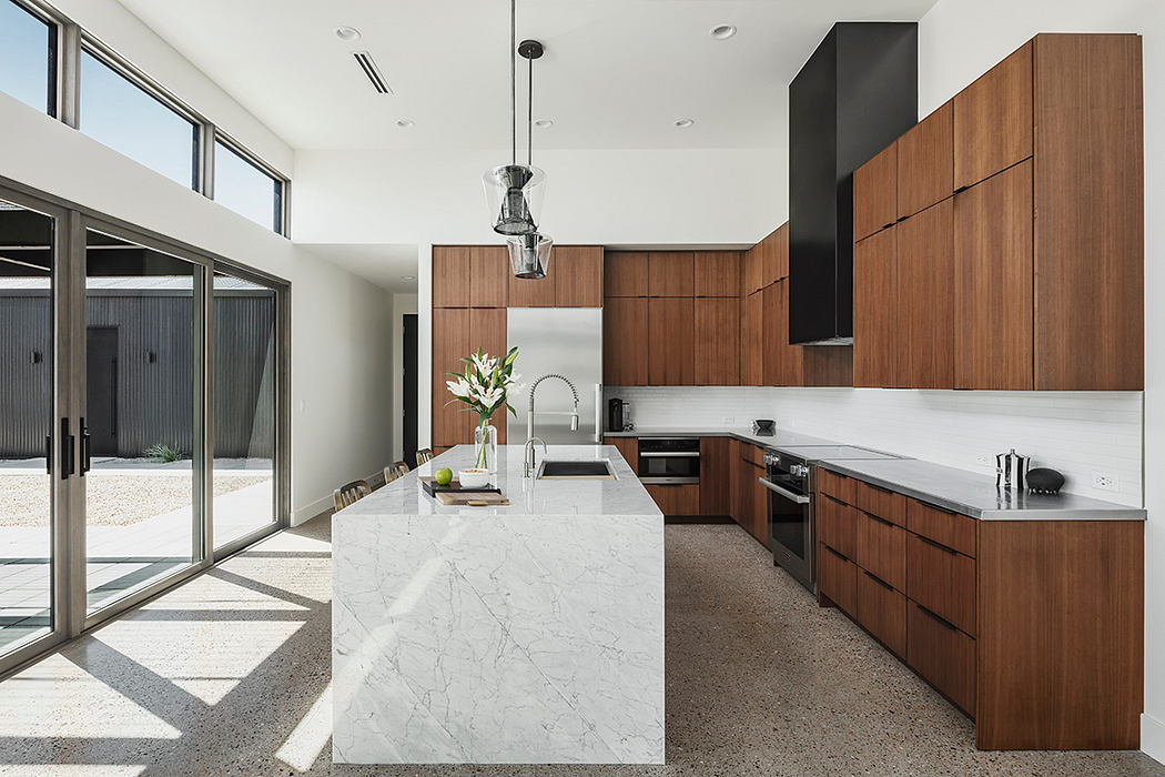 Sleek and modern kitchen with marble island, warm wood cabinetry, and large windows.