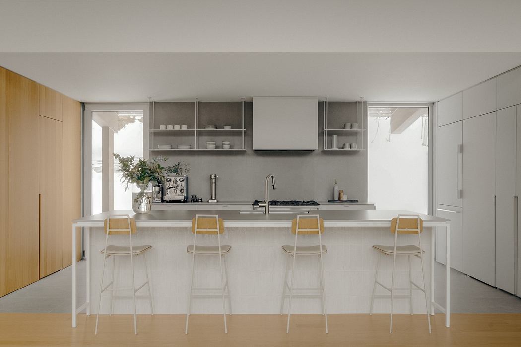 Minimalist kitchen with streamlined cabinetry, open shelving, and a long countertop with bar stools.