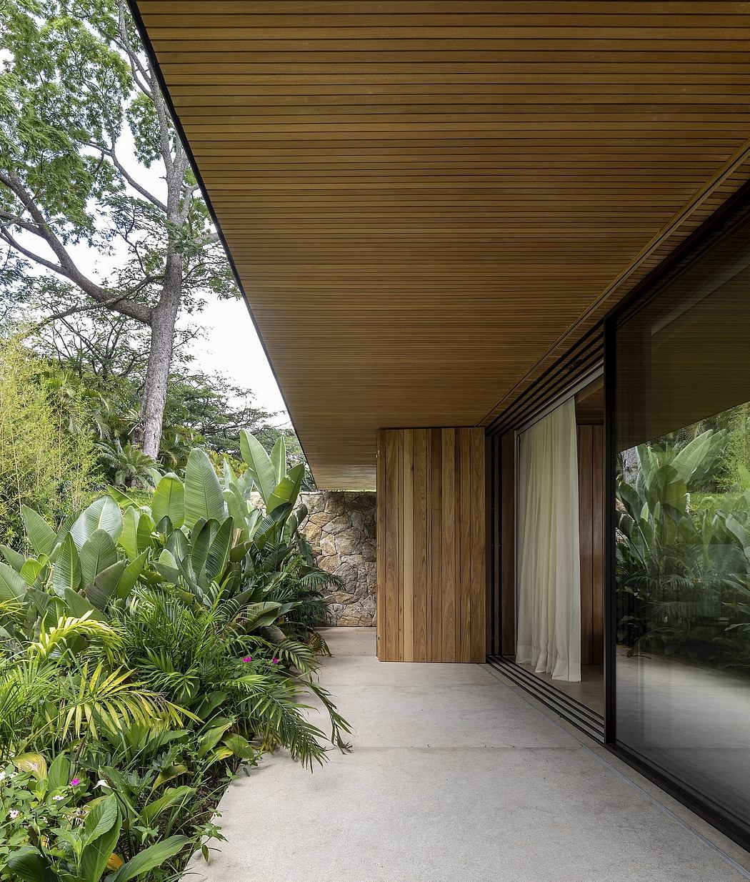 A wooden-paneled exterior with large sliding glass doors leading to a lush tropical garden.