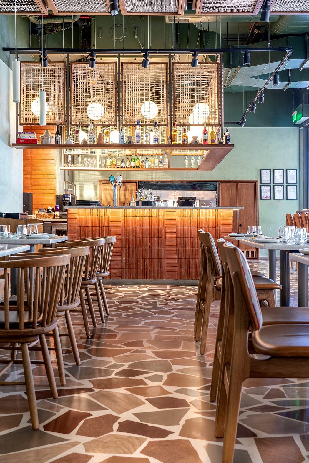 Rustic-modern bar interior with wooden furniture, patterned floor tiles, and pendant lights.