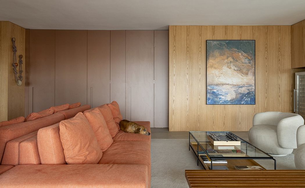 A modern living space featuring warm-toned wood paneling, plush coral sofas, and a striking abstract artwork.