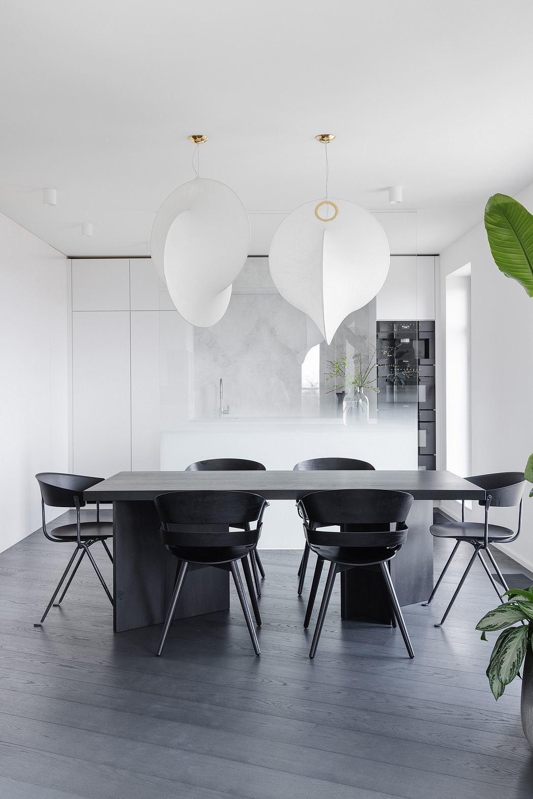 Minimalist dining room with sleek black chairs, circular pendant lights, and glimpse of kitchen.