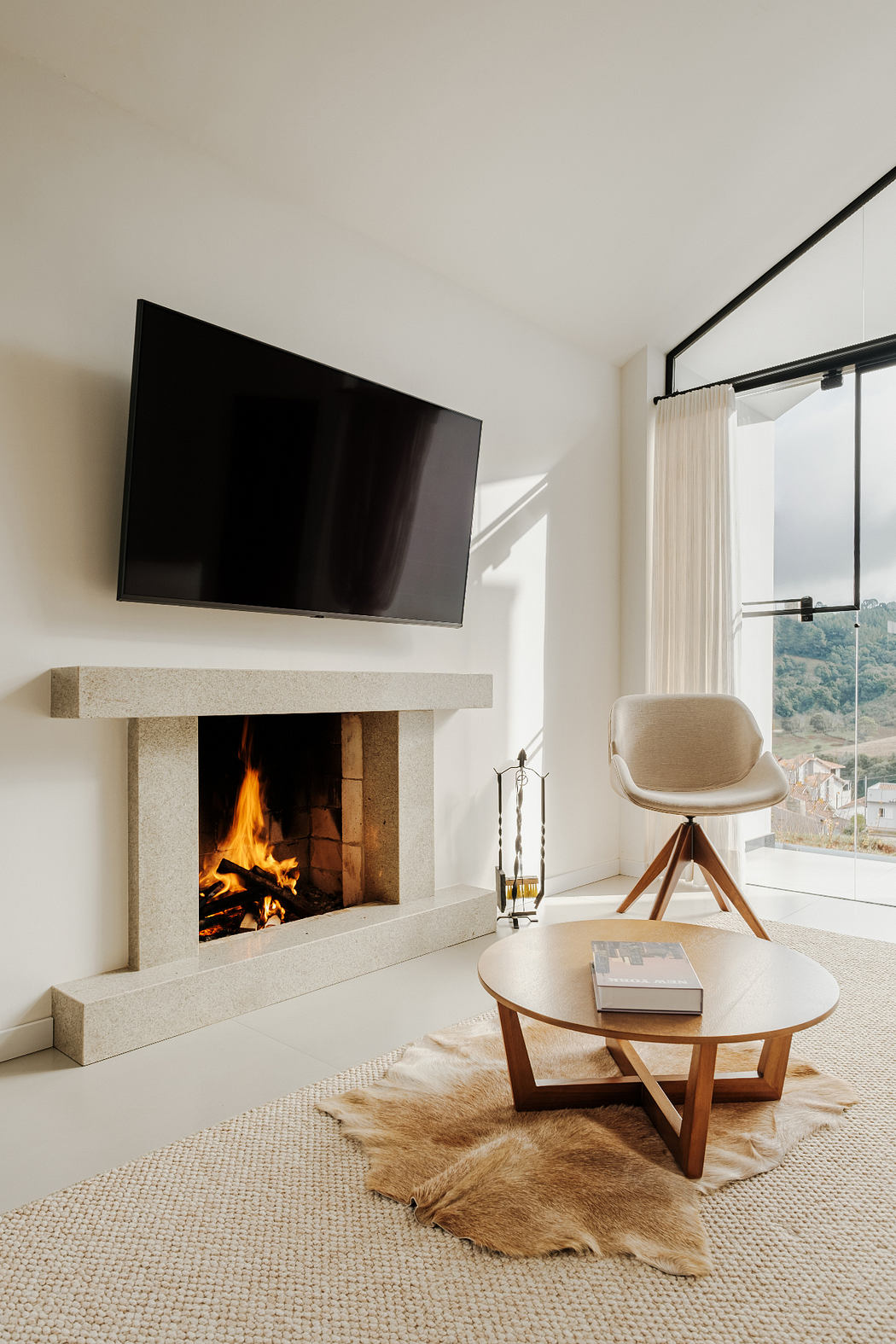 Modern living room with stone fireplace, TV, and cozy furnishings overlooking a scenic view.